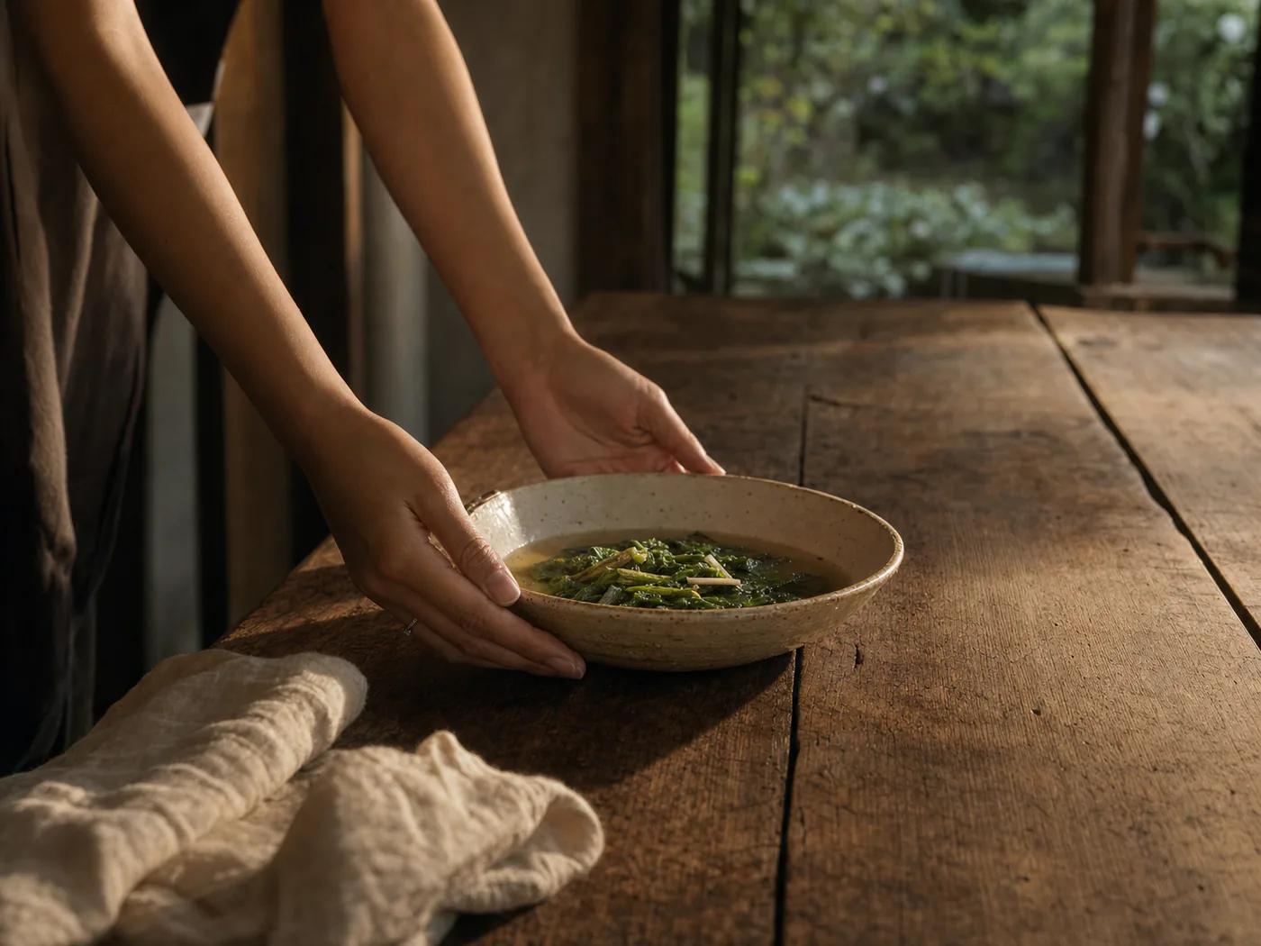 Hands setting a shared dish onto a long timber table.