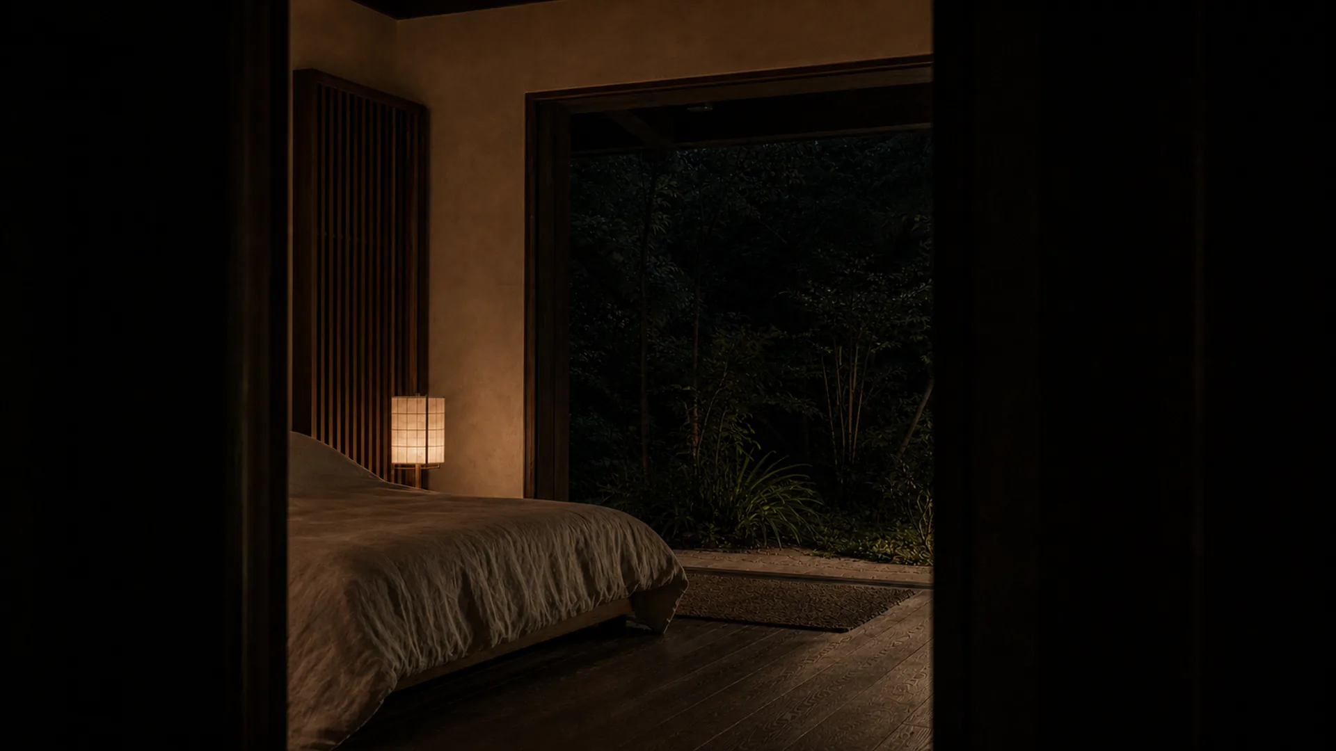 A room at night with one low lamp and the garden dark beyond the glass.